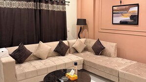 A modern living room with a beige sectional sofa, a black coffee table, a ceiling fan, and a framed picture on the wall. - 1 BHK Apartment, View , Bharia Phase 7, Balcony , Parking , Private and Secure (Islamabad)