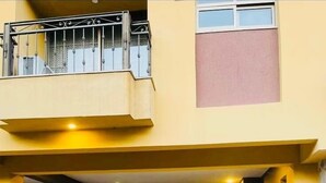 Une voiture Honda argentée est garée dans un abri-voiture d’un immeuble à deux étages, doté d’un balcon et où l’on peut voir un extincteur.