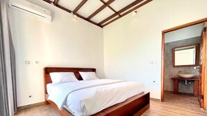 A bedroom with a wooden bed, a built-in bench, a bathroom with a sink and mirror, and a ceiling fan. - Villa Loba (Denpasar)