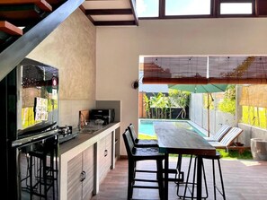 Eine moderne Küche mit Bar, einem Esstisch mit Stühlen und Blick auf Pool und Garten.