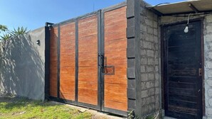 A large wooden gate with a metal frame, a concrete wall, and a black door with a light bulb hanging above it. - Villa Loba (Denpasar)