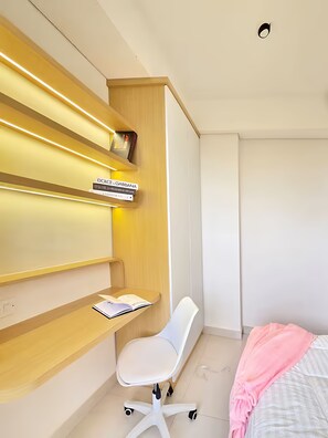 Une chambre moderne avec un bureau en bois, une chaise blanche et un lit recouvert d’une couverture rose.