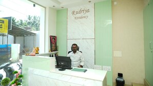 Egy recepciós pult, rajta egy számítógéppel, egy képkeretben elhelyezett képpel és egy „Rudriya Residency” felirattal ellátott táblával.