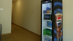Egy Pepsi logóval ellátott, különböző italokkal feltöltött automata található egy folyosón, melynek csempézett a padlója és egyszerű a falak kialakítása.