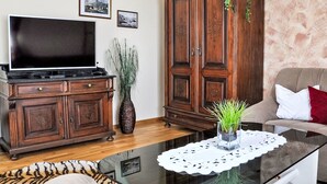 Una sala de estar con televisor de pantalla plana, un mueble de madera y una mesa de centro de cristal con un mantel de encaje.