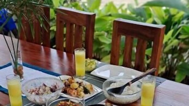 A wooden dining table with plates of food, glasses of juice, and a bowl of cereal. - Banks Boutique Inn Kampala (Kampala)