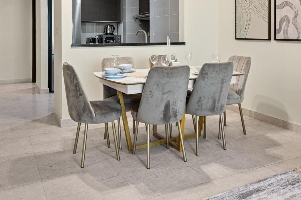 A dining area with a table set for four, featuring grey upholstered chairs with gold legs.