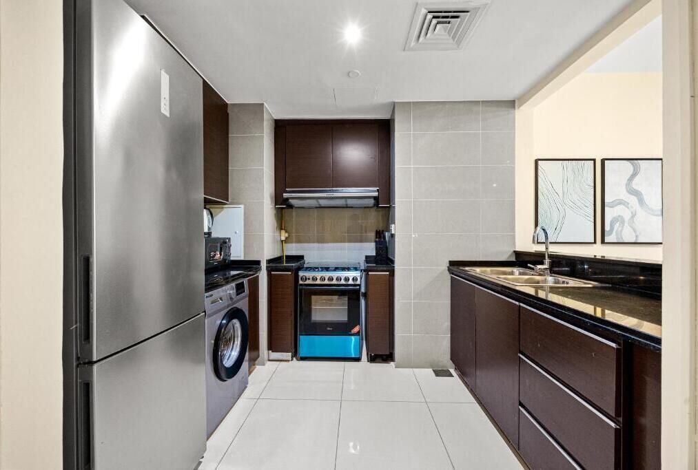 Eine kompakte Küche mit einem Edelstahl-Kühlschrank, einer Waschmaschine, einem blauen Backofen und einem Spülbecken mit schwarzer Arbeitsplatte.