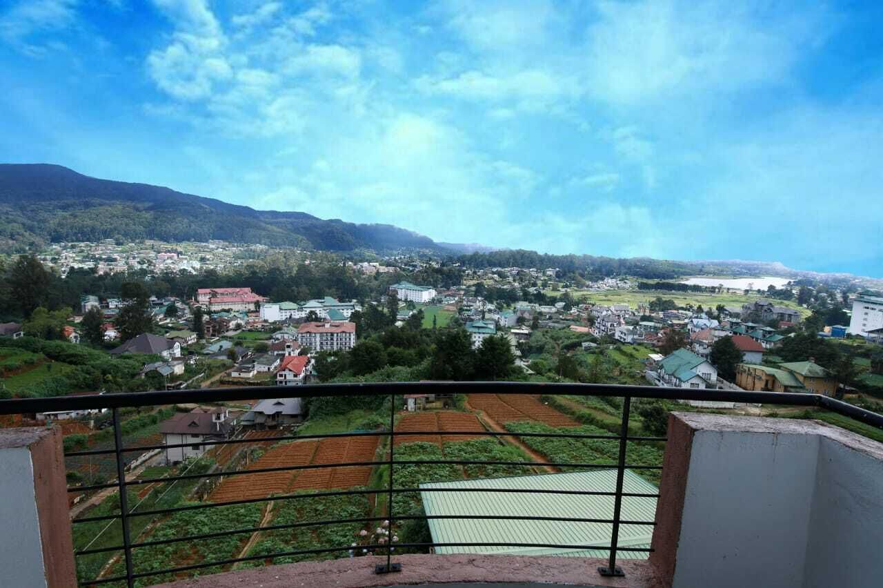 A panoramic view of a town with residential buildings, green fields, and mountains in the background.
