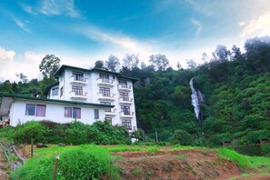 Un edificio blanco de varios pisos con balcones, rodeado de exuberante follaje y una cascada.