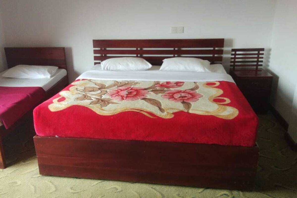 A room with a large bed, a smaller bed, a nightstand, and a wooden headboard.