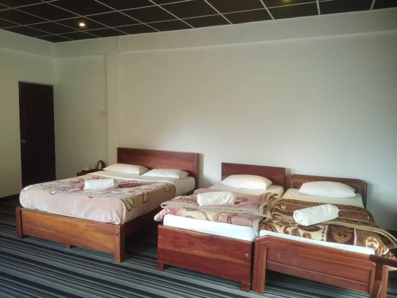 Une chambre d’hôtel avec deux lits en bois, une moquette à rayures et un mur blanc uni.