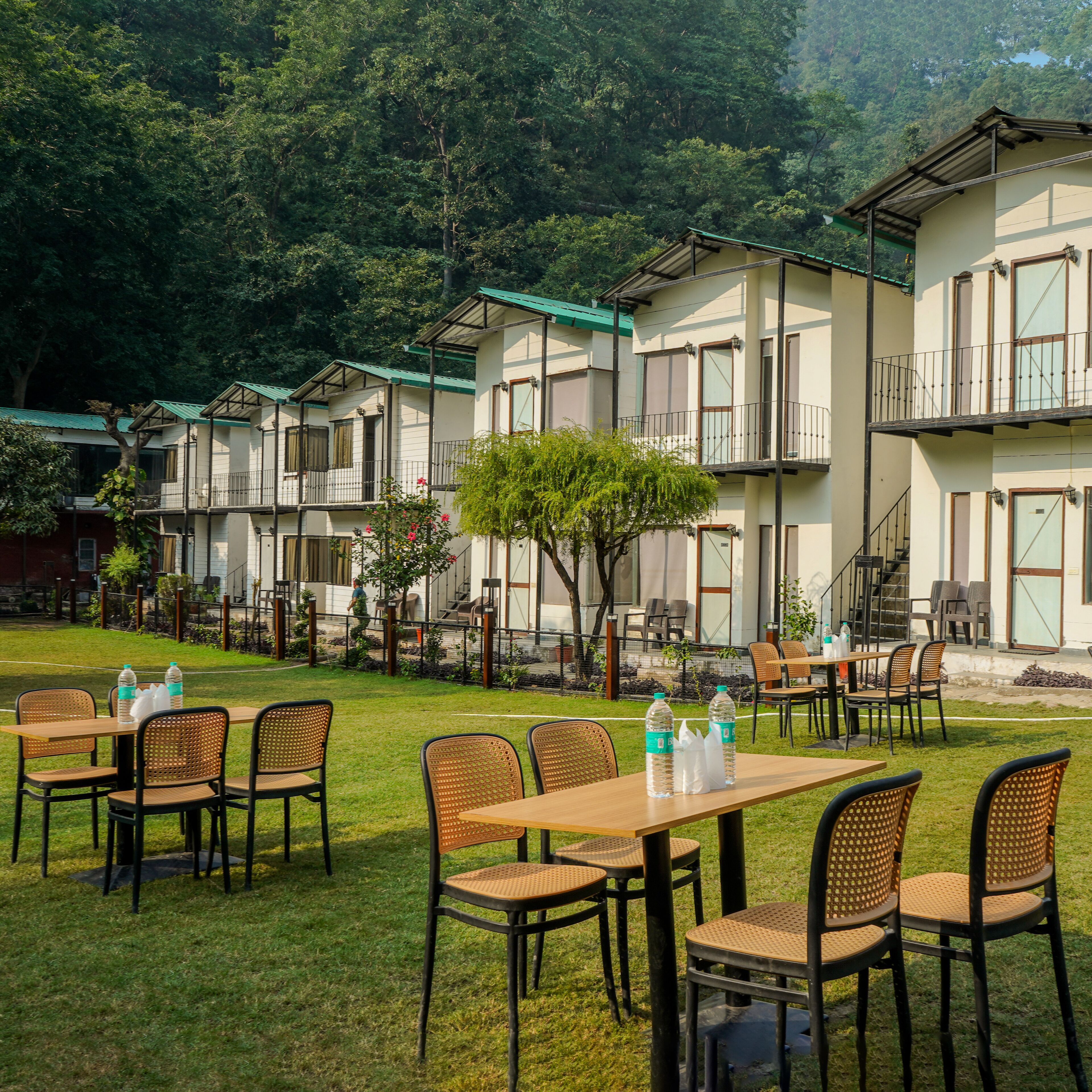 A hotel with outdoor seating, multiple floors, and a lush green backdrop.