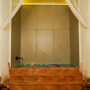 A bathroom with a wooden floor, a tiled wall, a black faucet, and a small plant.