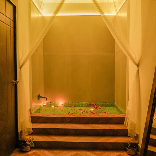 A bathroom with a bathtub, a shower, and a sink. There are rose petals on the floor and a small plant on the sink.