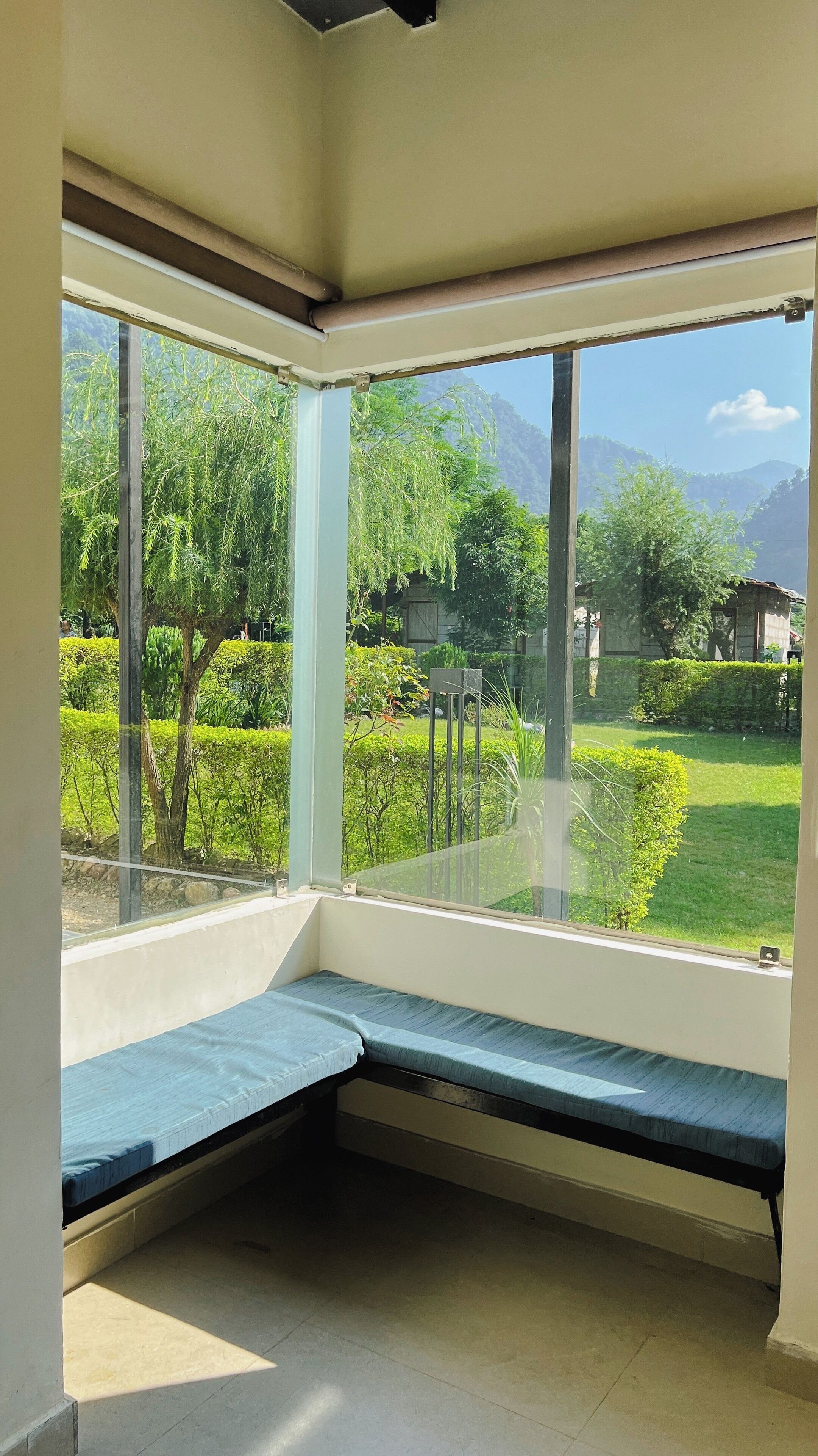 Una habitación con un ventanal grande, una banca y vistas a un jardín y montañas.