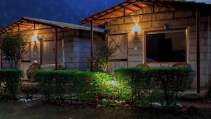 Un edificio rustico con tetto in legno e pareti in pietra, caratterizzato da un'ampia finestra e un piccolo portico con una sedia.