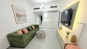 Ein modernes Wohnzimmer mit einem grünen Sofa, einem pinken Hocker, einem kleinen runden Tisch und einem an der Wand befestigten Flachbildfernseher.