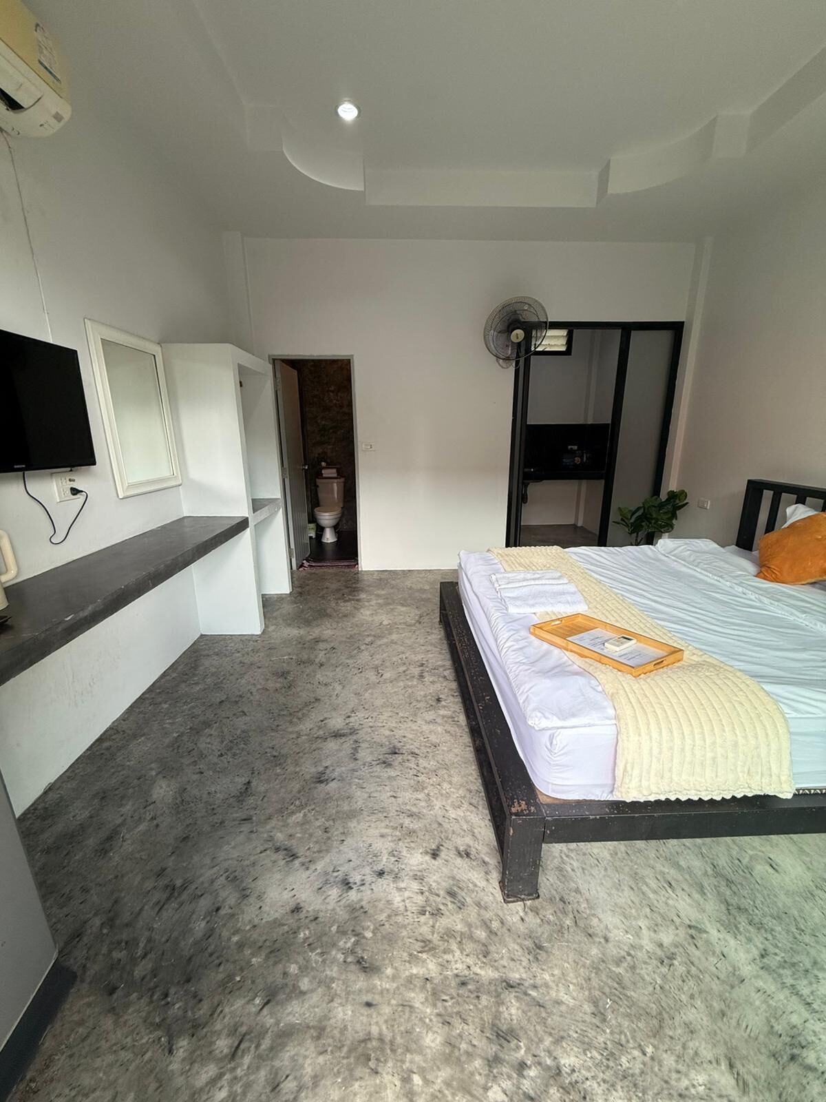Un dormitorio con cama, mesita de noche, televisor y ventilador de techo.