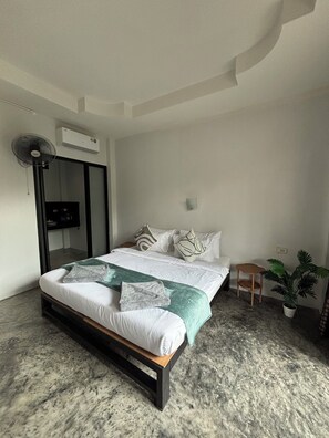 A modern bedroom with a large bed, a small table, a potted plant, and a ceiling fan. - Sairee Living Apartments (Ko Tao)