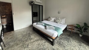 Een moderne slaapkamer met een bed, een klein tafeltje, een kamerplant en een badkamer met toilet en douche.