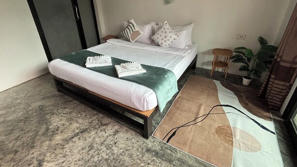 Uma cama bem arrumada com lençóis brancos e duas toalhas, um cobertor verde e um tapete marrom com um design simples.