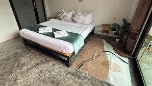 Quarto bem arrumado com cama, almofadas, uma mesinha e um vaso de planta.