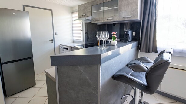 A modern kitchen with a built-in island, stainless steel appliances, and bar stools. - Welcome to Le Cocon Châtillonais apartment in the center of Châtillon sur Chalaronne (Châtillon-sur-Chalaronne)