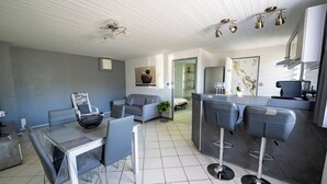 A modern kitchen with bar stools, a dining area with a table and chairs, and a living area with a sofa and a plant. - Welcome to Le Cocon Châtillonais apartment in the center of Châtillon sur Chalaronne (Châtillon-sur-Chalaronne)