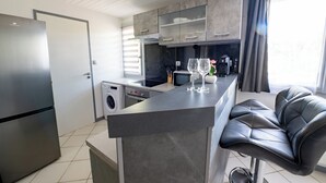A modern kitchen with a built-in washing machine, a refrigerator, and a bar area with a leather chair. - Welcome to Le Cocon Châtillonais apartment in the center of Châtillon sur Chalaronne (Châtillon-sur-Chalaronne)