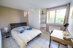 A bedroom with a bed, bedside table, lamp, chair, desk, shelves, and a window.