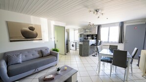 A modern living room with a grey sofa, a coffee table, and a dining area with a table and chairs. - Welcome to Le Cocon Châtillonais apartment in the center of Châtillon sur Chalaronne (Châtillon-sur-Chalaronne)