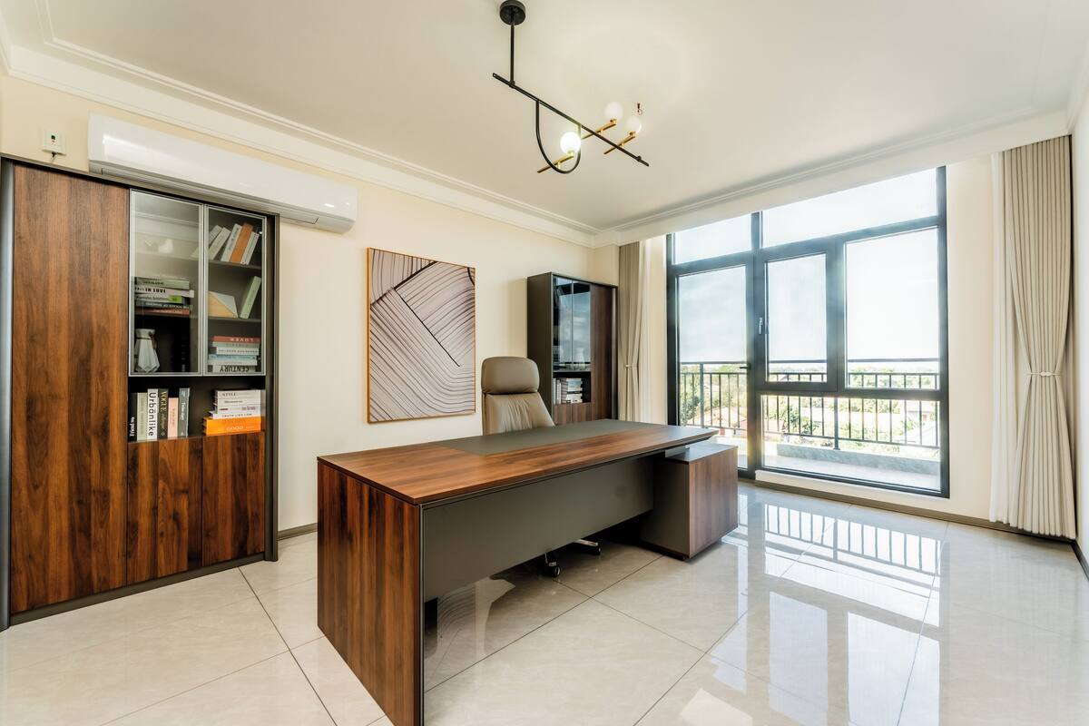 Un espacio de oficina moderno con un escritorio de madera, una estantería y un amplio ventanal con vistas.