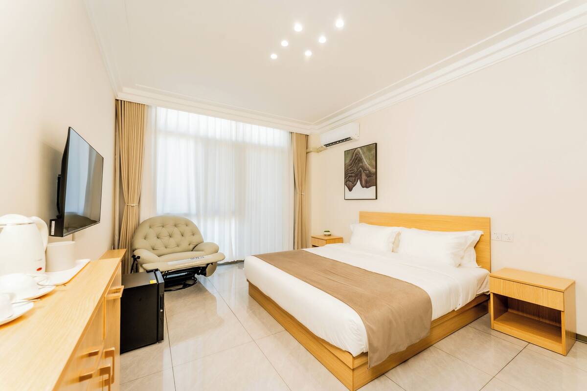Habitación de hotel con cama, escritorio con computadora, silla, televisor y ventana con cortinas.