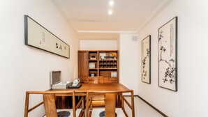 A traditional-style dining room with a wooden table and chairs, framed calligraphy art on the walls, and a wooden cabinet with shelves in the background. - Beijing Daxing Apartment  (Vientiane)