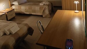 Una habitación de hotel con dos camas, un escritorio de madera, una silla, una mesita de noche y una lámpara.