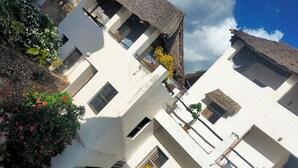 A white building with multiple windows and balconies, surrounded by greenery and a clear sky. - Jannat House Lamu (Lamu)