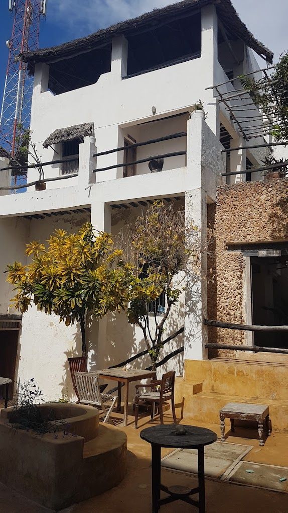 A two-story building with a balcony, outdoor seating, and a tree.