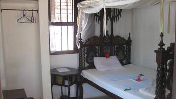 Un lit simple avec un baldaquin, un petit bureau et une chaise dans une pièce dotée d’une fenêtre.