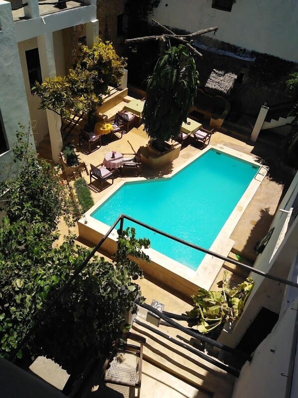 An outdoor swimming pool surrounded by lounge chairs and potted plants, with a staircase leading up to a building.