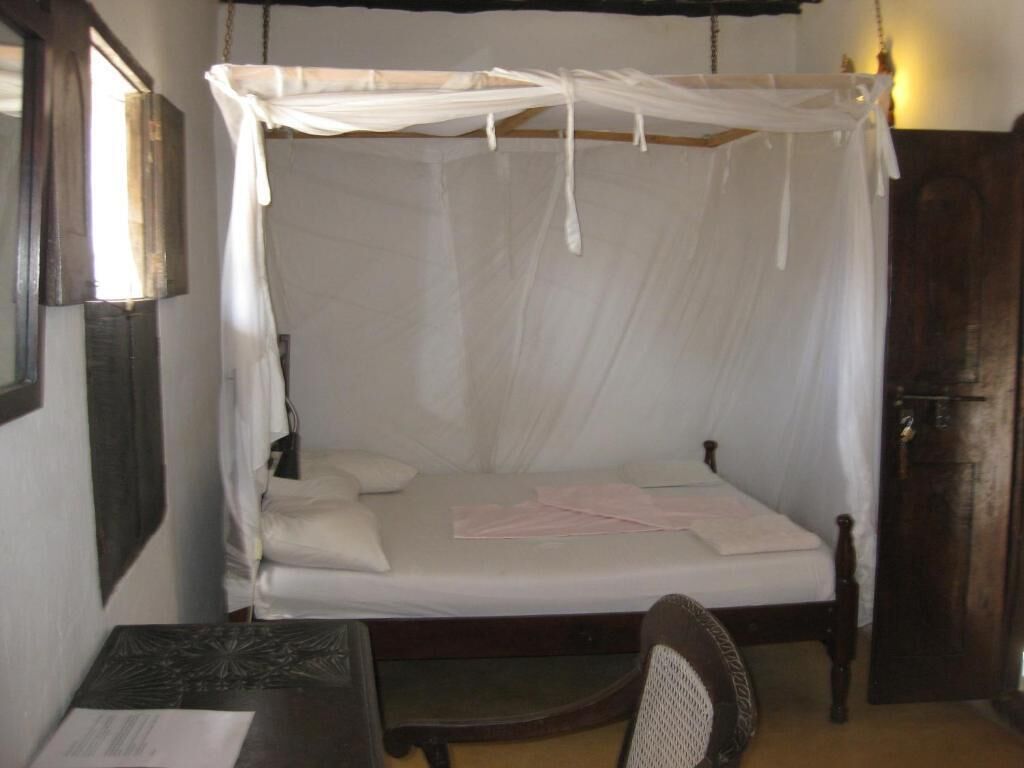A single bed with a canopy, a wooden nightstand, a chair, and a wardrobe.