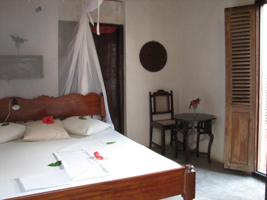 Una stanza con un letto, una sedia, un tavolo e una finestra con persiane in legno.