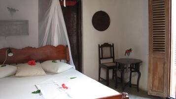 A room with a bed, a chair, a table, and a window with wooden shutters.