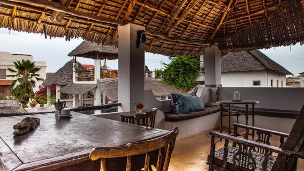An outdoor seating area with a thatched roof, wooden furniture, and a view of surrounding buildings. - Jannat House Lamu (Lamu)
