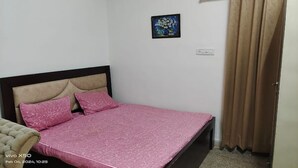 Ein Schlafzimmer mit Bett, Kopfstück, Wandsteckdose und einer mit Vorhängen versehenen Tür.