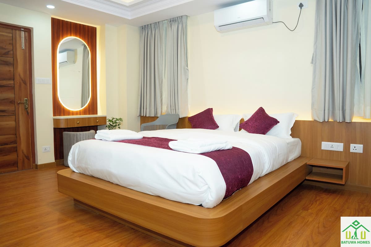 A modern hotel room with a large bed, wooden headboard, and a built-in vanity with a mirror.