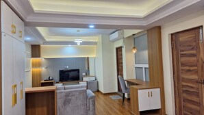 A modern living room with a flat-screen TV, grey sofa, wooden cabinets, and a wooden door. - Batuwa Homes (Kathmandu)
