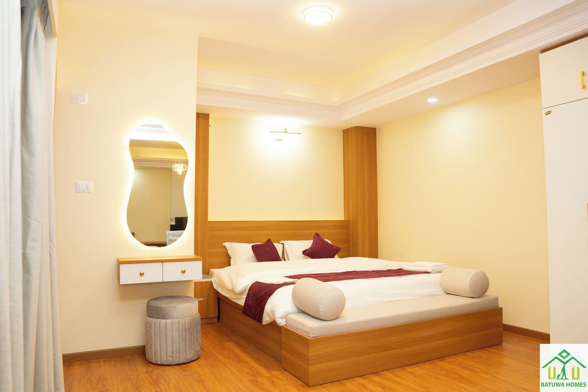 A bedroom with a wooden bed, bedside table, mirror, and a small round stool.