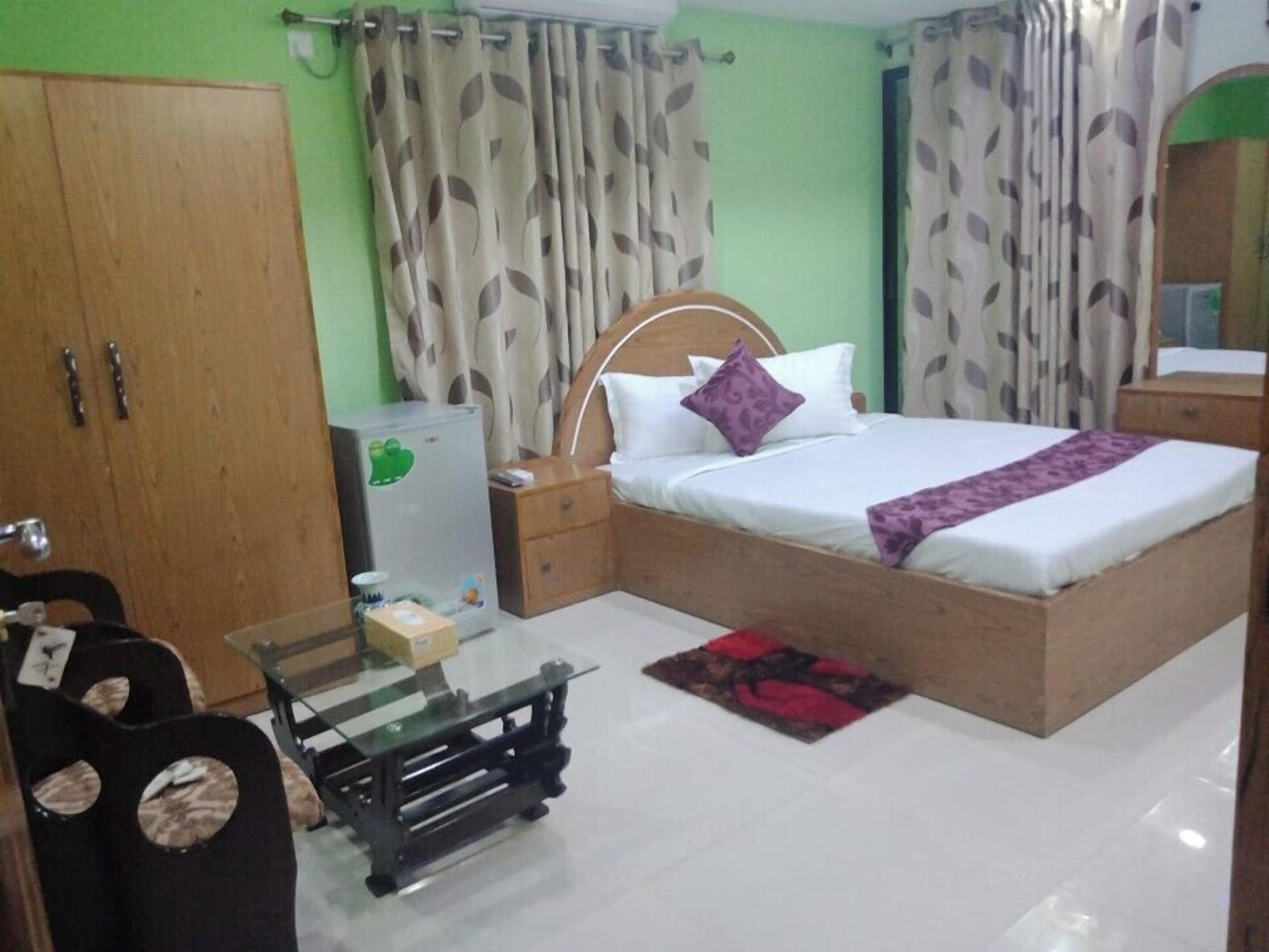 A bedroom with a bed, nightstand, wardrobe, and a glass table.