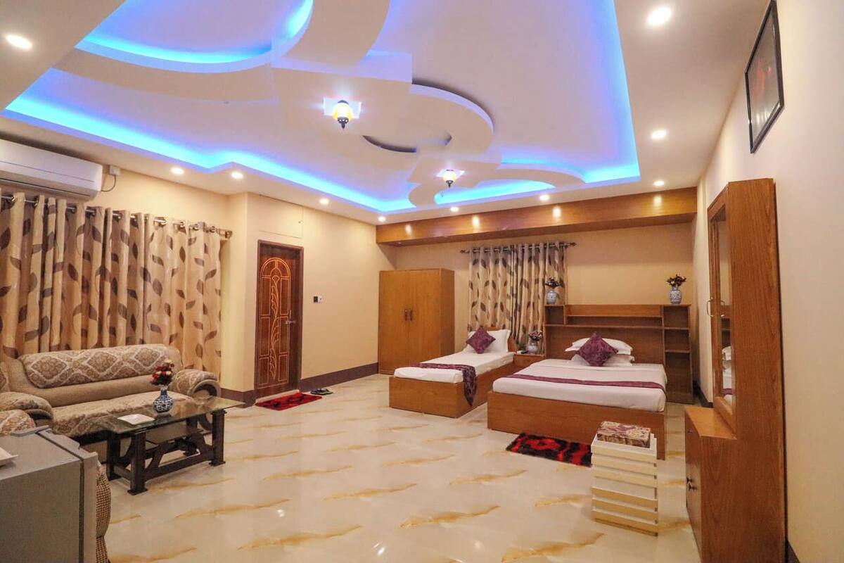 Un dormitorio moderno con sofá, dos camas, un armario de madera e iluminación empotrada en el techo.